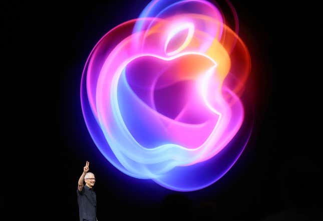 Tim Cook sostiene un símbolo de la paz frente a un gran gráfico de una manzana que se muestra detrás de él.