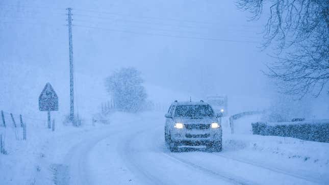 A photo of a silver SUV driving through a snow storm. 