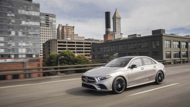 A photo of a silver Mercedes A Class sedan driving through a city. 