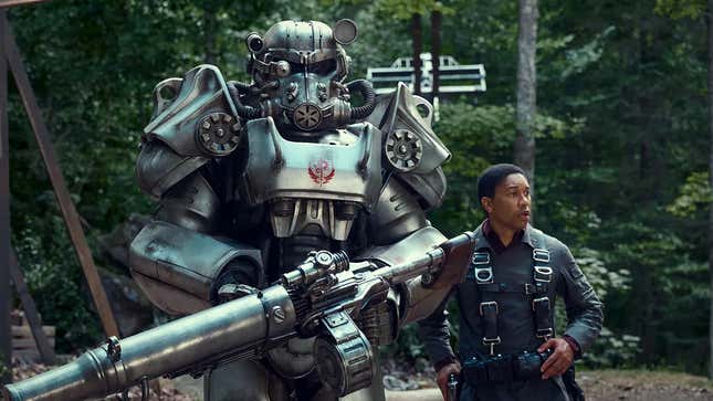In a promotional image for the Fallout TV show, a figure wearing Fallout power armor stands next to a person.