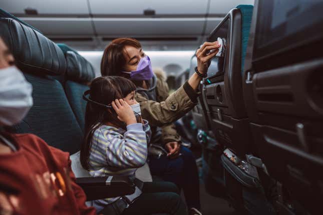 Three passengers sit on an airplane wearing surgical masks.
