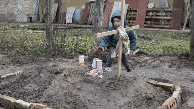 A young kid gives an offering of food to the grave of a woman in the town of Bucha, on the outskirts of Kyiv, on April 4, 2022.