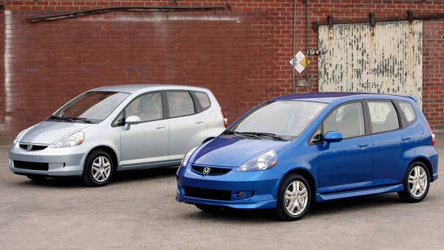 Front-quarter view of a silver and blue first-generation Honda Fit parked side by side.