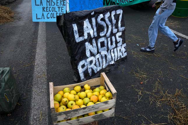 Apples are made available next to a poster reading &quot; Let us produce&quot; as farmers block highway, Thursday, Feb.1, 2024 in Argenteuil, north of Paris. France&#39;s two major farmers unions announced Thursday their decision to suspend protests and lift road blockades across the country, in a dramatic development shortly after the French prime minister unveiled a new set of measures they see as &quot;tangible progress.&quot; Farmers have been protesting for days across the country to denounce low wages, heavy regulation and unfair competition from abroad. (AP Photo/Michel Euler)