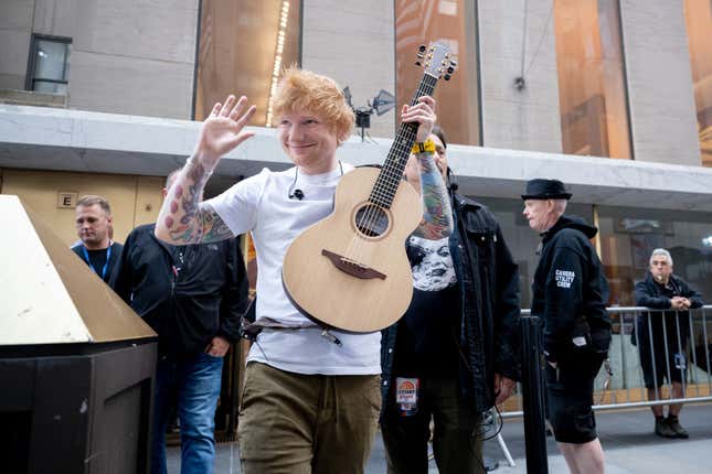 Ed Sheeran hält eine Akustikgitarre in der Hand und winkt den Fans zu