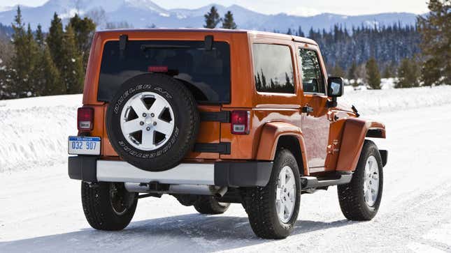 A photo of an orange Jeep Wrangler parked on the snow. 