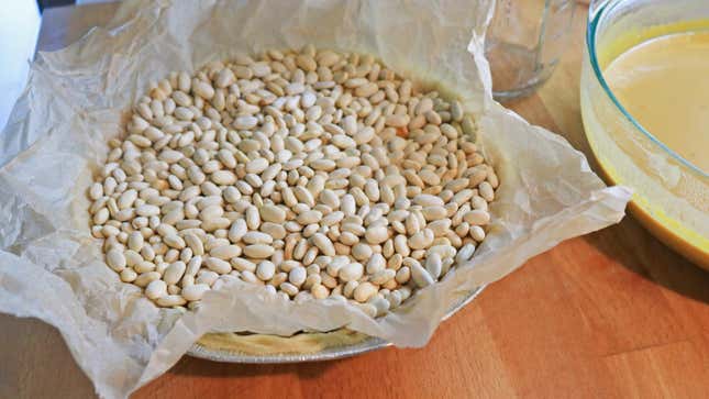 A pie crust with a parchment paper liner and baking beans inside.