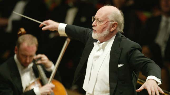 John Williams, dressed in a tuxedo, conducts an orchestra.