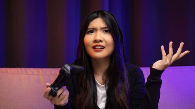 A woman stares at the camera while holding a controller in a confused pose.