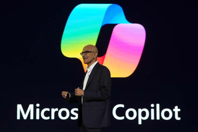 Satya Nadella wearing a business suit speaking in front of a backdrop with the Microsoft Copilot logo