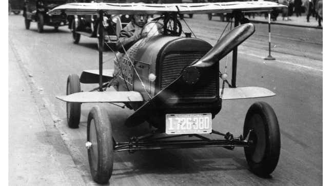 A black and white photo of a car with wings and a propellor. 