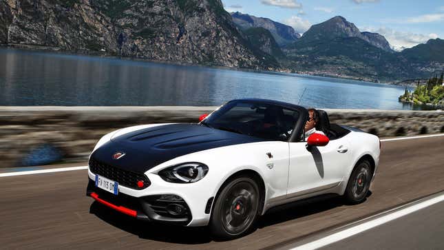 A white Fiat 124 Abarth driving top down in front of a lake and mountains