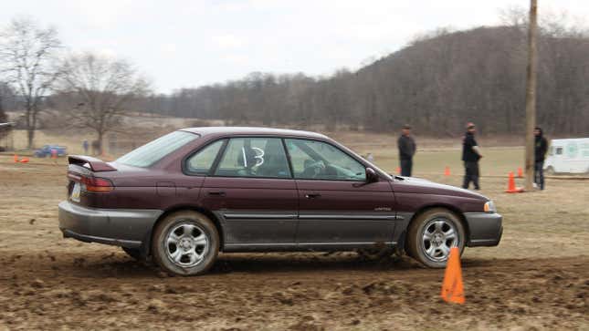 the side view of a maroon legacy SUS driving on mud