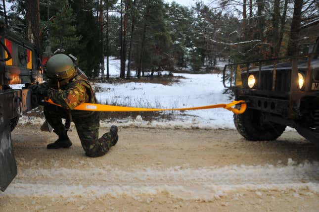 A Romanian soldier attaching a tow strap to a Humvee