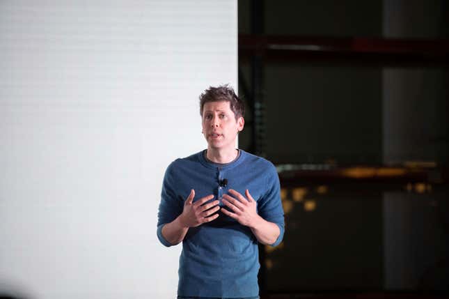 Sam Altman speaking with his hands up wearing a dark blue shirt in front of a backdrop