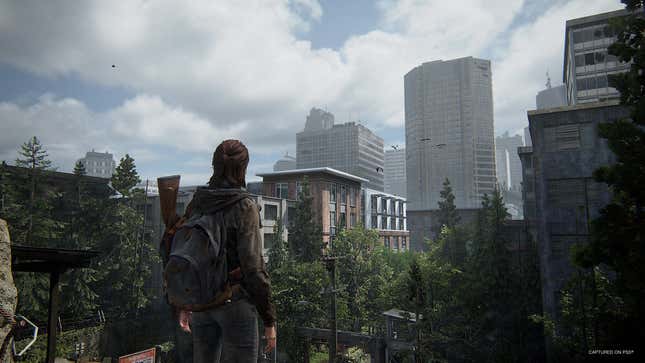 Protagonis Eli berdiri di depan reruntuhan pusat kota Seattle di The Last of Us Part II.