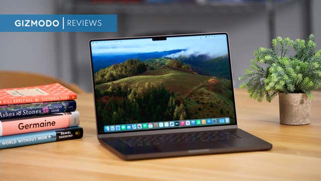 A black M3 Max Powered MacBook Pro next to a stack of books and a planter.