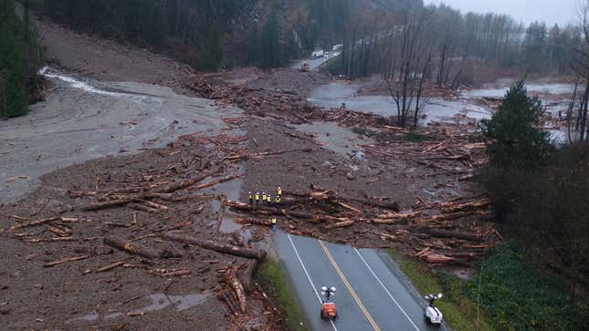 An aerial look at a debris flow that crosses a road as a crew of workers looks at the damage.