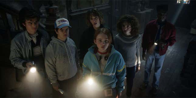 The teenage cast of Netflix's Stranger Things inside an old mansion and staring at something with their flashlights. 