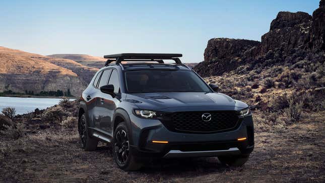 a dark gray Mazda CX-50 parked on dirt in front of a lake and rock formations