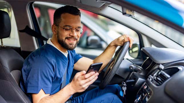 Eine Krankenschwester in ihrer OP-Kleidung sitzt in ihrem stehenden Auto mit geöffnetem Fenster.