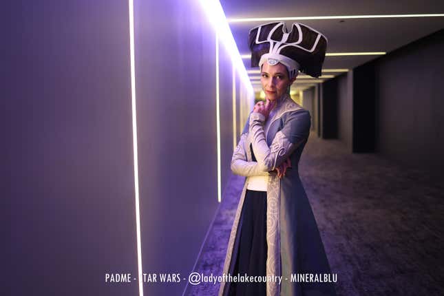 A Padme Amidala cosplayer stands with her hand on her chin. 