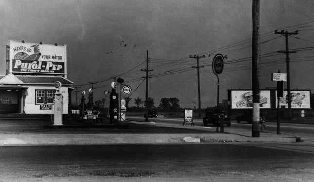 A black and white photo of a gas station at a small town cross roads. 