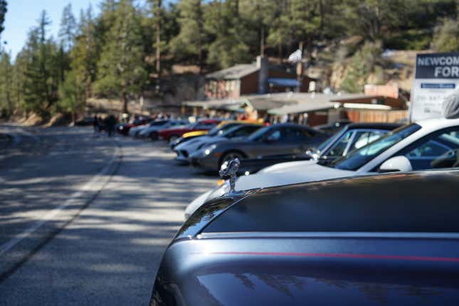 A Rolls-Royce Phantom hood with the Spirit of Ecstasy exposed is parked in front of other cars.