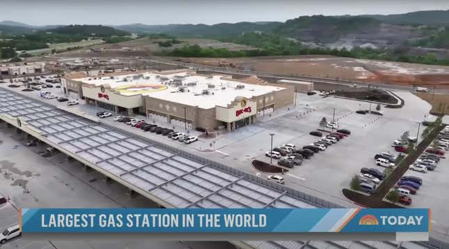 Overhead view of the largest gas station in the world--a Buc'ees in Tennessee. The smokey mountains rise in the background and the large parking lot is half full of cars. 