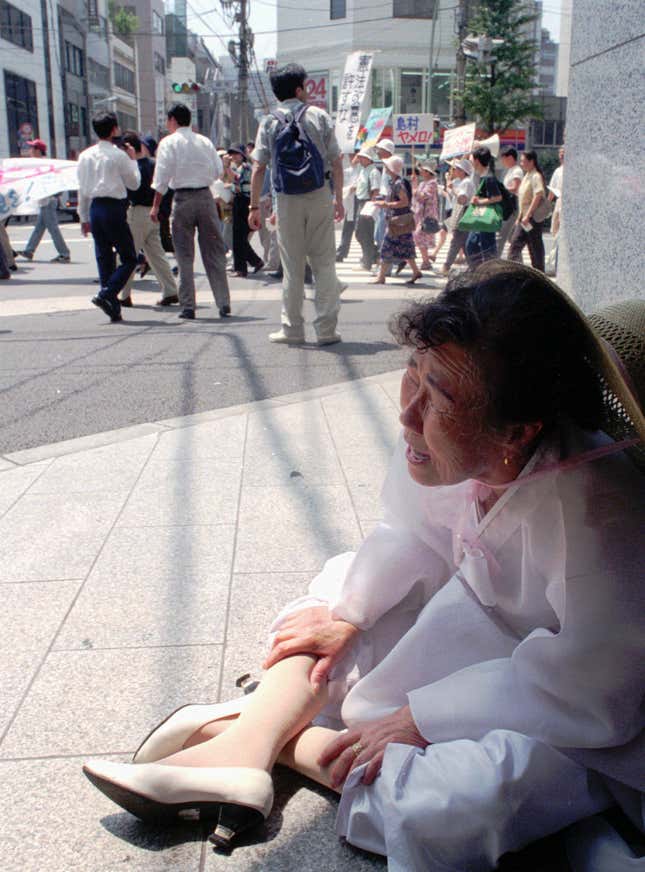 A former comfort woman crouches down on a Tokyo street corner during a protest march on the 50th anniversary of the end of World War II.