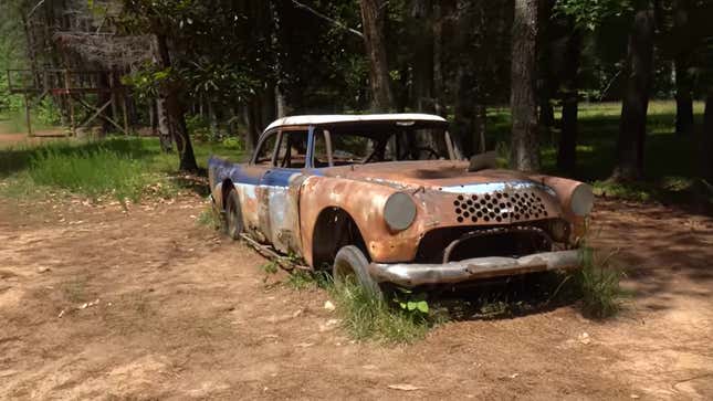 Una foto de un coche oxidado en el bosque. 