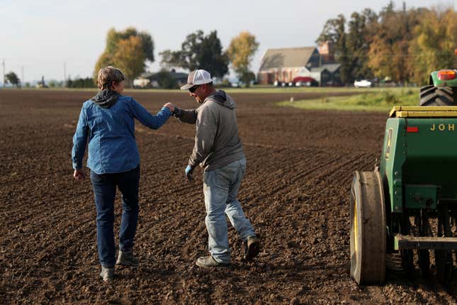 Gayle Goschie fist bumps Eloy Luevanos after setting up a harrow to be pulled behind a tractor and grain hopper in preparation for planting winter barley at Goschie Farms in Mount Angel, Ore., Tuesday, Oct. 31, 2023. Fall is the off-season, but recently, her farming team has been adding winter barley, a relatively newer crop in the world of beer, to their rotation. In the face of climate change, Goschie will need all the new strategies the farm can get to sustain what they produce and provide to local and larger breweries alike. (AP Photo/Amanda Loman)