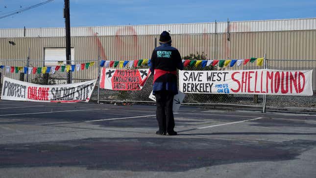 A person looks at signs hanging in a parking lot, the only undeveloped portion of the shellmound in West Berkeley where ancestors of today&#39;s Ohlone people established the first human settlement on the shores of the San Francisco Bay, in Berkeley, Calif., Wednesday, March 13, 2024. Berkeley&#39;s City Council voted unanimously Tuesday, March 12, 2024, to adopt an ordinance giving the title of the land to the Sogorea Te&#39; Land Trust, a women-led, San Francisco Bay Area collective that works to return land to Indigenous people and that raised the funds needed to reach the agreement. (AP Photo/Jeff Chiu)