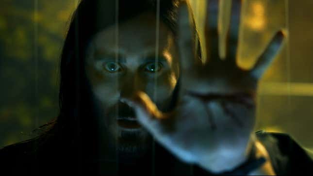 Jared Leto in a scene from Morbius with a bloody hand stretched out towards a cave. 