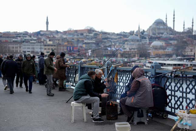 People warm themselves with a fire while fishing over the Galata bridge in Istanbul, Turkey, Wednesday, Feb. 21, 2024. Turkey&#39;s central bank left its key interest rate unchanged at 45% on Thursday, pausing a series of aggressive rate hikes aimed at taming high inflation. (AP Photo/Khalil Hamra)