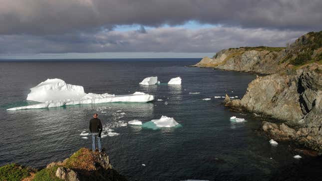 A man gazes across the North Atlantic under a darkly cloudy sky. Bright white fragments of icebergs float by.  