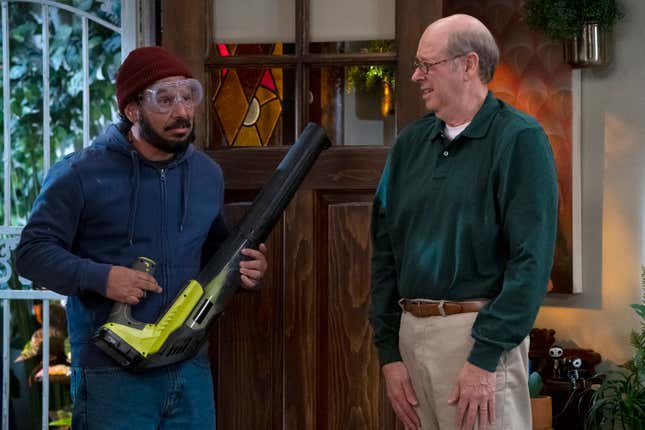 A man wearing safety googles and a beanie holding a leafblower next to an older man wearing khakis