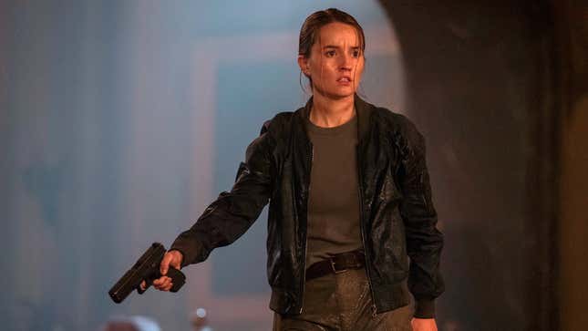 Abby points a gun to her right as she looks at something off-screen.