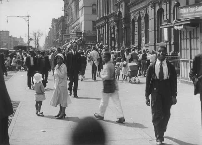 Busy street in Harlem, New York, New York, 1929. ‘Free Milk Fund for Babies’ at right. Possibly Lenox Avenue, looking south from just south of 130th Street, as identified by church spires. 