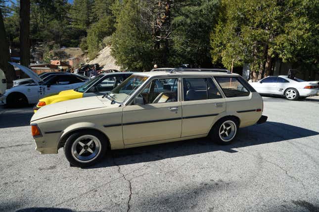 A beige 1980s Toyota Corolla wagon is parked among other enthusiast cars.