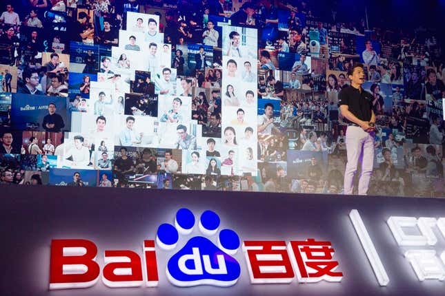 Robin Li speaking on stage, a Baidu logo is displayed at the bottom of the stage, and the letters AI are shaped by photos of people on the backdrop behind Li