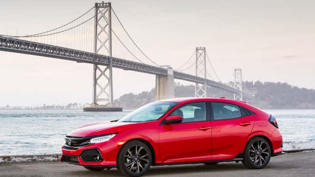 A photo of a red Honda Civic Hatchback parked in front of a bridge. 