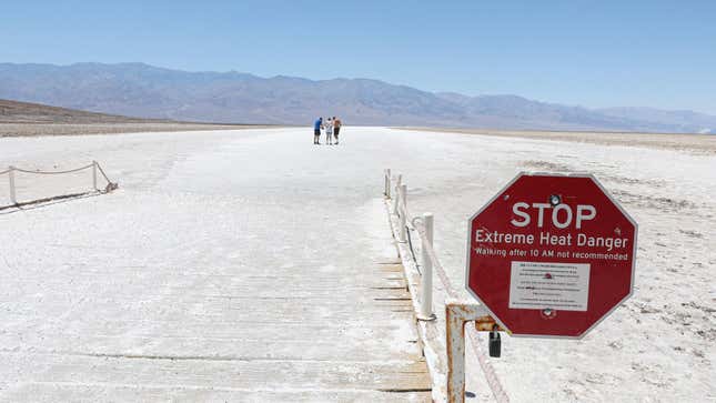 A heat warning sign is displayed as people walk on the salt flats at Badwater Basin in Death Valley National Park.