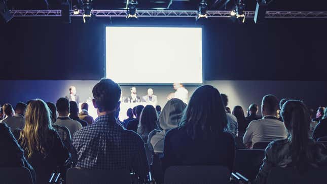 An audience watches a panel at a conference