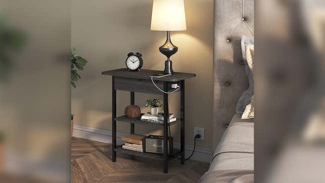 An end table against the wall with a phone charger plugged into its built-in outlets.