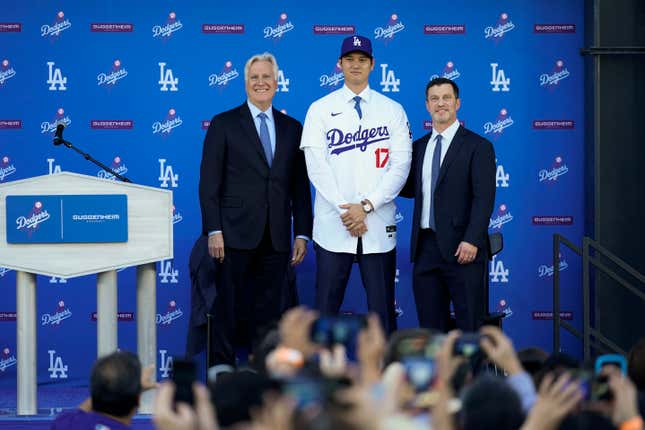 Los Angeles Dodgers&#39; Shohei Ohtani, center, poses for a photo with owner and chairman Mark Walter, left, and president of baseball operations Andrew Friedman applaud during a news conference at Dodger Stadium Thursday, Dec. 14, 2023, in Los Angeles. (AP Photo/Ashley Landis)