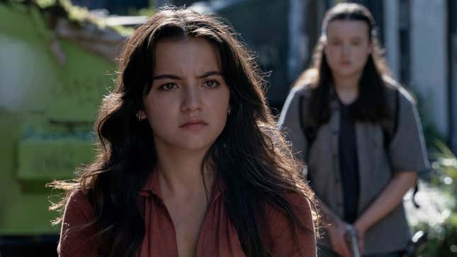 Dina looks at something off-screen while Ellie approaches her from behind.