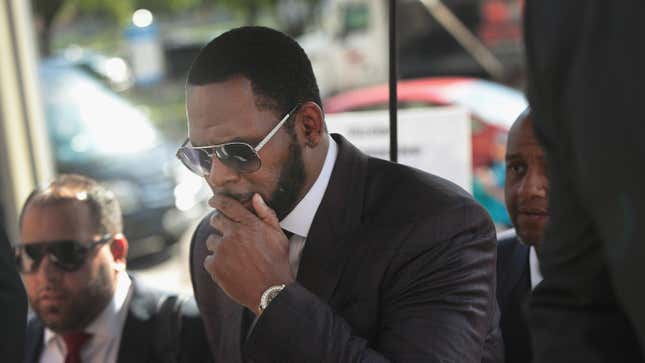 R. Kelly covers his mouth as he speaks to members of his entourage as he arrives at the Leighton Criminal Courts Building for a hearing on June 26, 2019. 