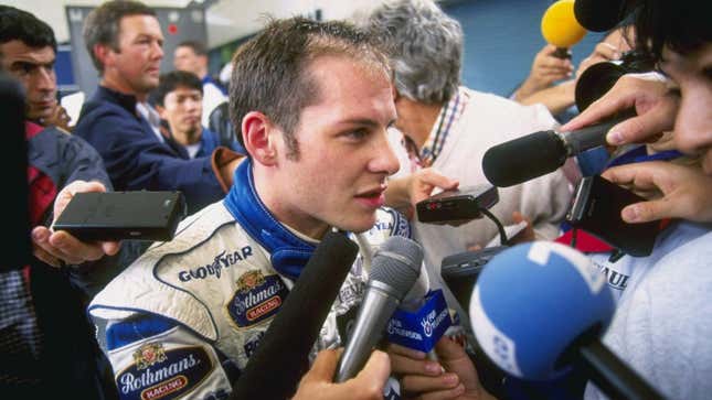 Jacques Villenueve speaks to reporters after blowing a tire during the 1996 Japanese Grand Prix. Crucially, he does not appear to be singing.