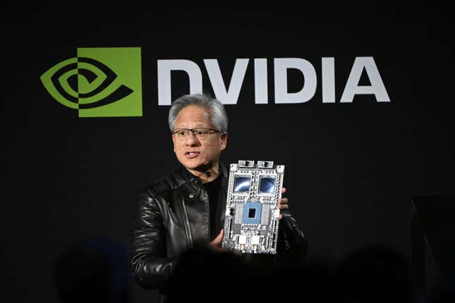 Jensen Huang speaking while holding up a chip platform in front of a black backdrop with the Nvidia logo